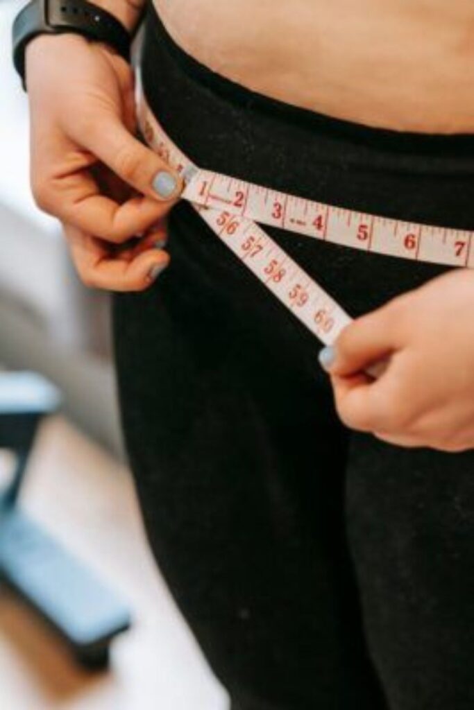 a petite lady measuring her hips with a tape